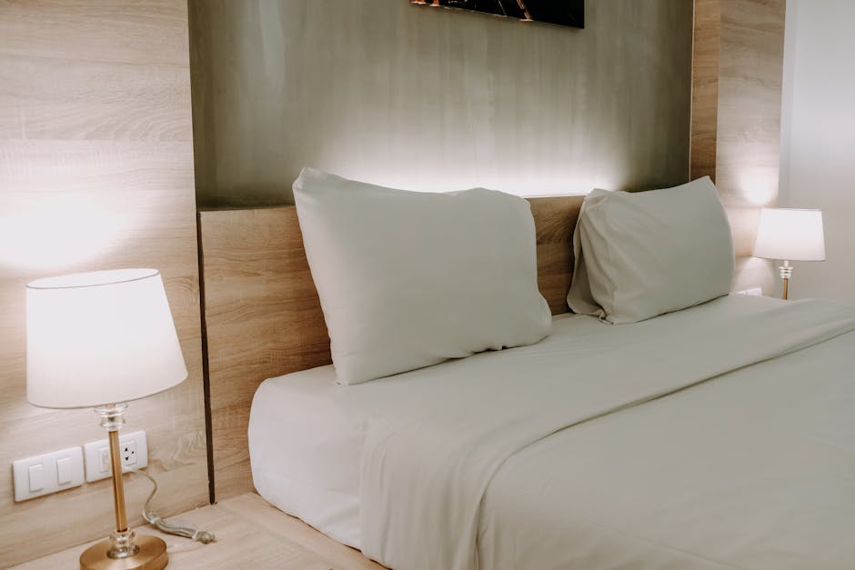 A modern bedroom with a minimalist design featuring a cozy bed with neutral bedding and warm ambient lighting.