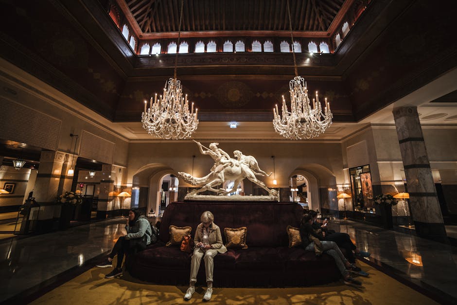 Unrecognizable people sitting on comfortable sofa in spacious hall of luxury hotel with crystal chandeliers and marble statue