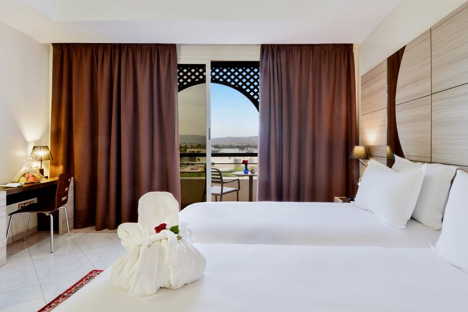 A modern hotel guestroom featuring custom-designed wooden casegoods, a upholstered accent chair, and a sleek desk, illustrating the strategic cost to furnish a hotel.