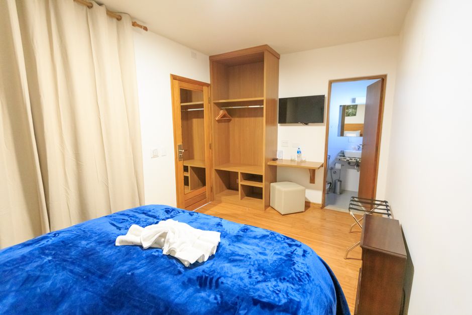 A modern hotel room with wooden furnishings, blue bedding, and a clean bathroom.