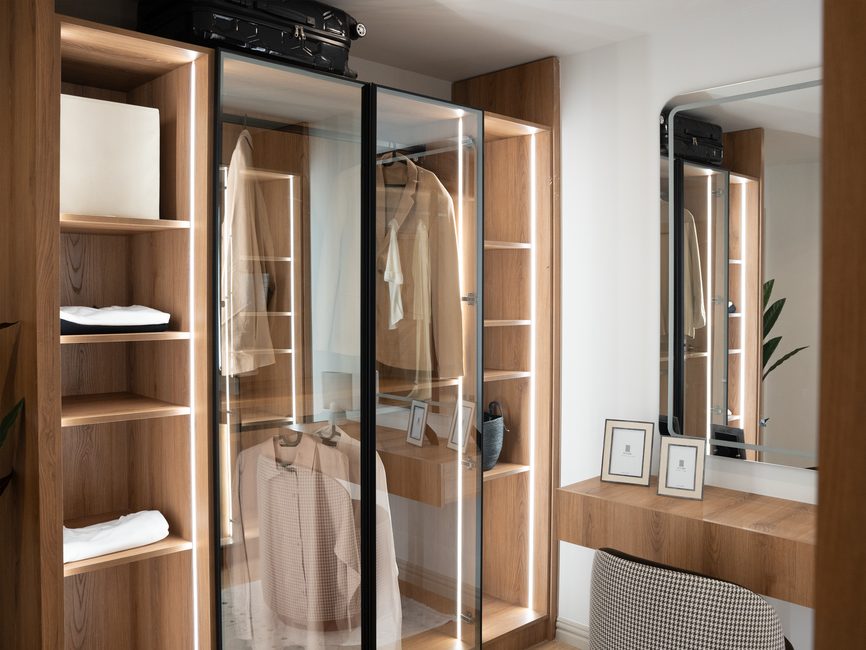 Modern hotel room with a sleek, minimalist built-in hotel wardrobe price in dark wood veneer and integrated lighting.