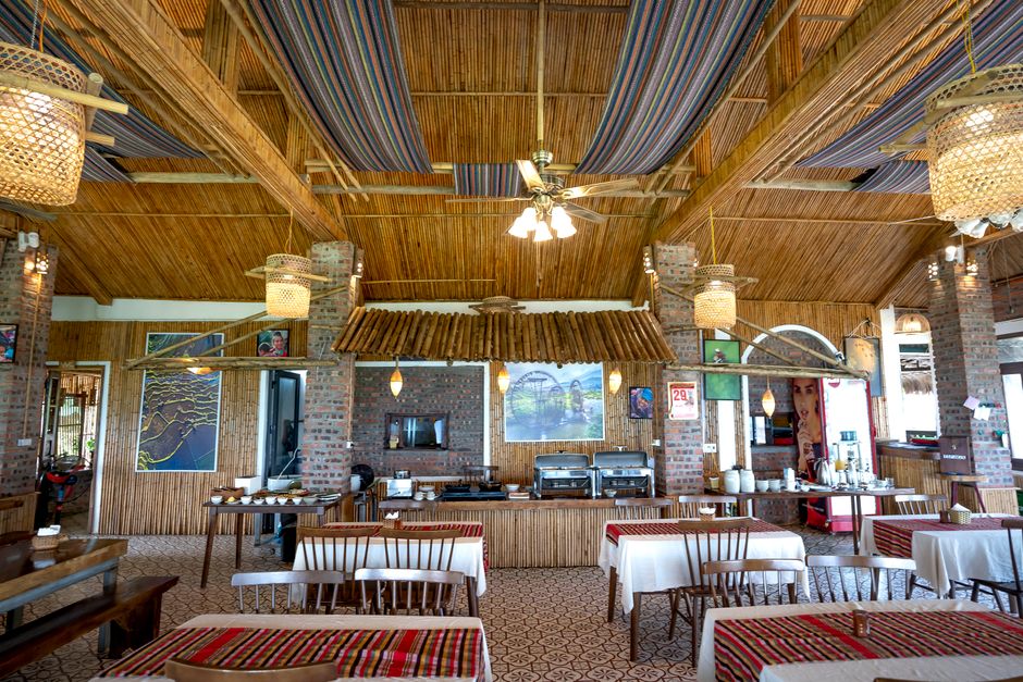 Tables with chairs against wall with paintings and counter with modern appliances in spacious cafeteria with wooden ceiling and hanging lamps