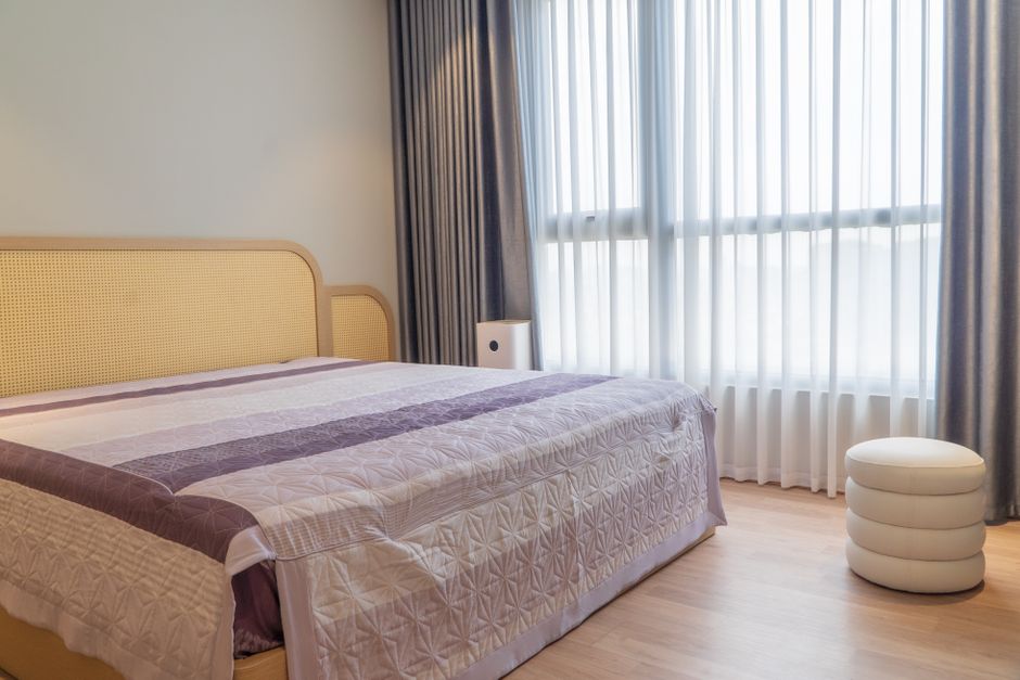 A neatly furnished modern hotel room featuring a bed, curtains, and soft lighting.