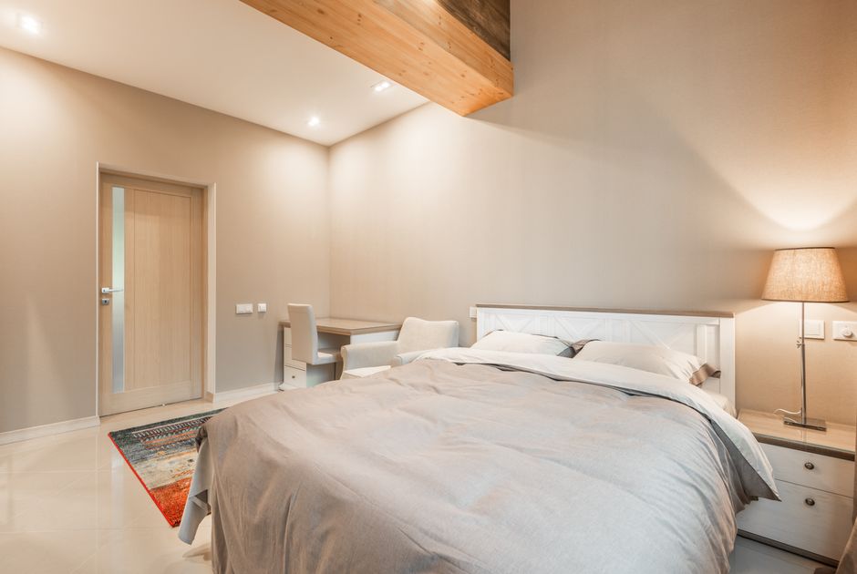 Interior of modern light bedroom with comfortable bed with lamp on bedside cabinet and desk with chair