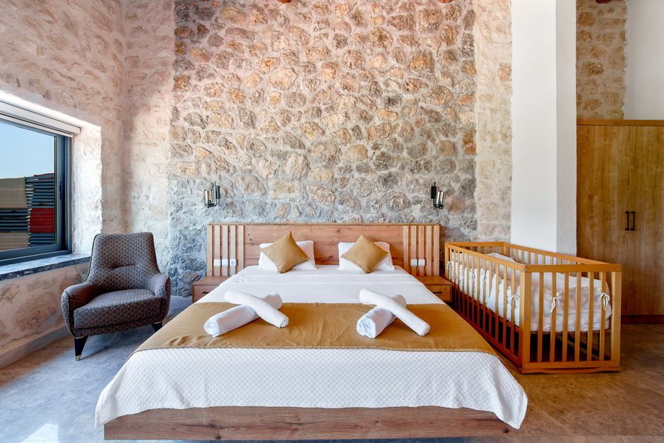 Inviting rustic bedroom featuring stone walls, a comfortable bed, and a wooden crib.